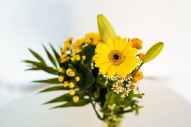  Gerbera çiçeği, kasımpatı, zambak. Sonbahar çiçekleri beyaz masada cam bir fincanda.