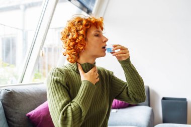 Sıcak yün yeşil kazaklı genç kızıl saçlı kadının portresi. Sıcak battaniyeyle örtülmüş. İlaç alıyor, soğuk enfeksiyon kapmış.