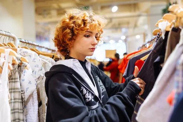 Kızıl saçlı çekici bir kadının portresi mağazada kıyafet deniyor, sonbahar kıyafetleri alıyor, alışveriş yapıyor.