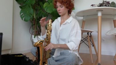 Genç kızıl saçlı bayan müzisyen yerde oturup müzik aleti saksafonu çalmaya hazırlıyor. Rüzgar müzik aleti, müzik eğitimi.