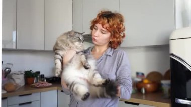 Parlak mutfakta kızıl saçlı genç bir kadın bebek gibi yumuşak kollarını ve kayalarını nazikçe tutuyor. Evcil hayvanla samimi bir ev hayvanı.