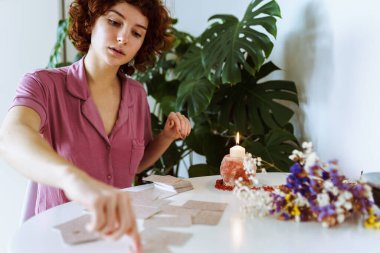 Genç kızıl saçlı kadın evinde oturmuş, falcılık kartları hazırlıyor.