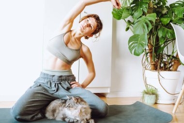 Genç atletik kadın kedisiyle yoga yapıyor.