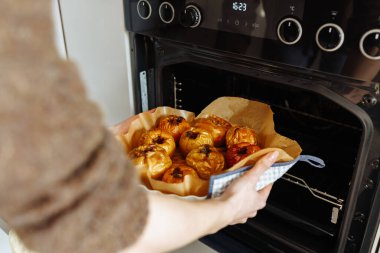 Kadın elleri ev mutfağındaki fırından fırınlanmış elmalarla tavayı kaldırıyor.