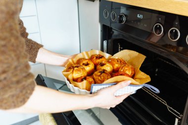 Kadın elleri ev mutfağındaki fırından fırınlanmış elmalarla tavayı kaldırıyor.