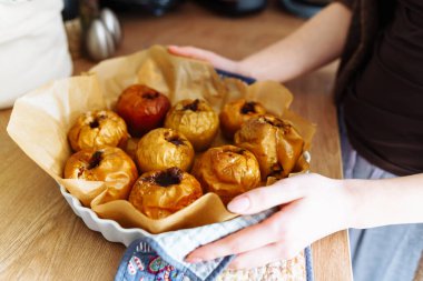 Kadın elleri ev mutfağındaki fırından fırınlanmış elmalarla tavayı kaldırıyor.