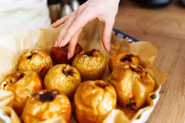 Genç kadınların elleri tarçınlı ve şekerli fırınlanmış elmayı yuvarlak tavadan alır.