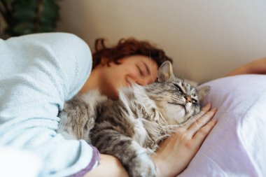 Yatakta kedisiyle uyuyan genç bir kadın. Bir evcil hayvanla arkadaşlık