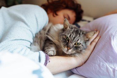 Yatakta kedisiyle uyuyan genç bir kadın. Bir evcil hayvanla arkadaşlık