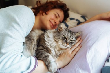Yatakta kedisiyle uyuyan genç bir kadın. Bir evcil hayvanla arkadaşlık