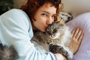 Yatakta kedisiyle uyuyan genç bir kadın. Bir evcil hayvanla arkadaşlık