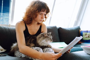 Genç bir kadın evdeki kanepede kedisiyle oturuyor.