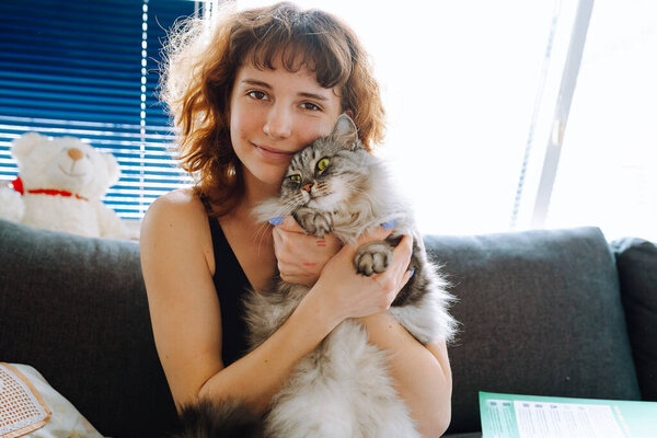 young red-haired woman hugging gray fluffy pet cat