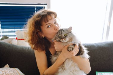 Genç kızıl saçlı kadın Gri tüylü kediyi kucaklıyor