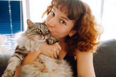 Genç kızıl saçlı kadın Gri tüylü kediyi kucaklıyor