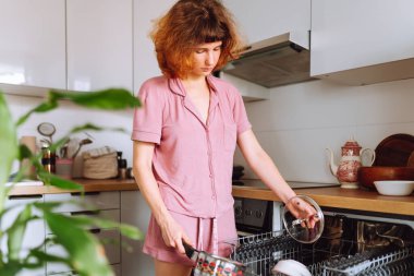 Bulaşık makinesi kullanan genç bir kadın bulaşık yıkıyor.