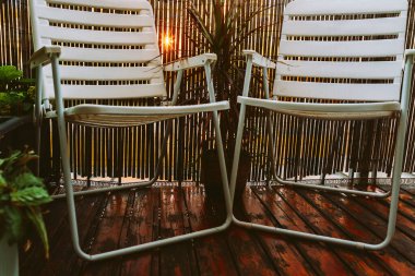 Terasta, ahşap zemin ve bahçe bitkileri olan plastik bahçe sandalyeleri.