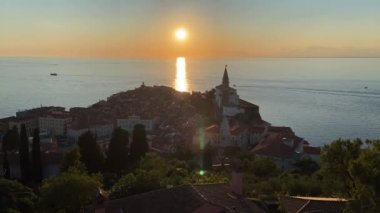 Piran, Slovenya. 31.10.2022. Tarihi merkezin kırmızı çatılarının manzarası. Ana kilisesi olan eski Piran kasabası. Günbatımı gökyüzü ve mavi Adriyatik denizi. Hava manzaralı, Slovenya kıyısı. 