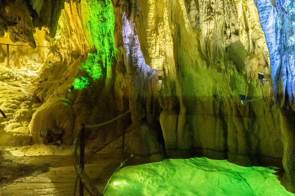 stock image Baar, Switzerland, April 29, 2023 Incredible fascinating rock formation and a small lake inside the Hoellengrotten cave illuminated with colorful lights