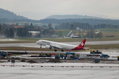 Zürih, İsviçre, 17 Ocak 2024 HB-AZK Helvetic Havayolları Embraer E195-E2 uçağı 28 numaralı pistten bir yağmur yağışı sırasında kalkıyor.