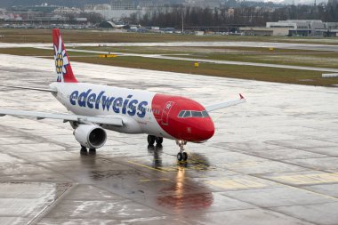 Zürih, İsviçre, 17 Ocak 2024 HB-JLR Edelweiss Air Airbus A320-214 bir yağmur yağmuru sırasında önlük boyunca hareket ediyor.