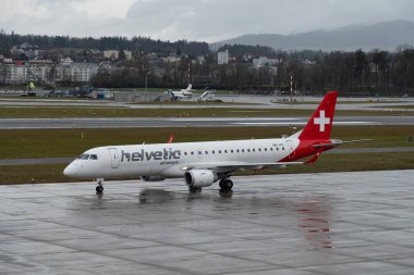 Zürih, İsviçre, 18 Ocak 2024 HB-JVX Helvetic Airways Embraer E190LR uçağı yağmur altında kapıya doğru ilerliyor.
