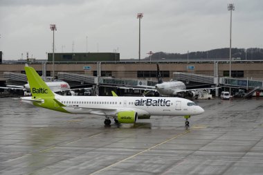 Zürih, İsviçre, 18 Ocak 2024 YL-ABE Hava Baltık Bombacısı CS-300 veya Airbus A220-300 uçakları yağmur altında kapıya doğru ilerliyorlar.