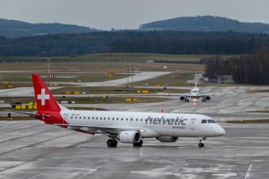 Zürih, İsviçre, 18 Ocak 2024 HB-JVY Helvetic Airways Embraer E190LR uçağı yağmur altında kapıya doğru ilerliyor.