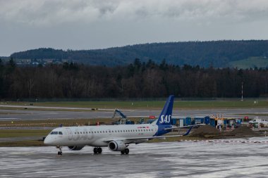 Zürih, İsviçre, 18 Ocak 2024 SE-RSK SAS İskandinav havayolları Embraer E195LR uçakları bir yağmur yağmuru sırasında önlük boyunca taksicilik yapıyor