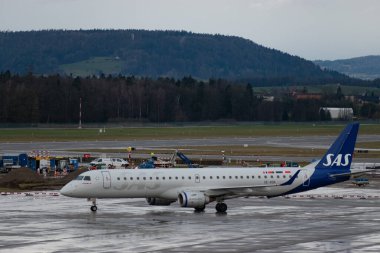 Zürih, İsviçre, 18 Ocak 2024 SE-RSK SAS İskandinav havayolları Embraer E195LR uçakları bir yağmur yağmuru sırasında önlük boyunca taksicilik yapıyor