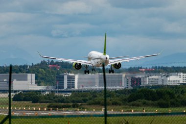 Zürih, İsviçre, 14 Eylül 2024 YL-AAAO Hava Baltık Bombacısı CS-300 veya Airbus A220-300 uçağı bulutlu bir günde 14 nolu piste iniyor.