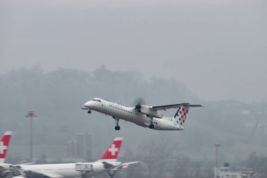 Zürih, İsviçre, 22 Ocak 2025 9A-CQA Hırvatistan Havayolları De Havilland Dash 8-400 uçağı yağmurlu bir günde 28 numaralı pistten kalkıyor.
