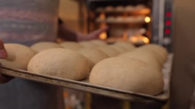 Bir kadın fırına çiğ çörekleri olan bir çarşaf koyar.