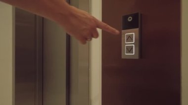 Modern apartmandaki asansör kapısının düğmesine elle basan adam.