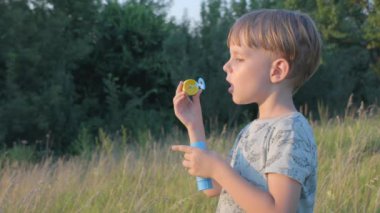 Gün batımında sabun köpüğü üfleyen küçük çocuk. Yavaş çekim.