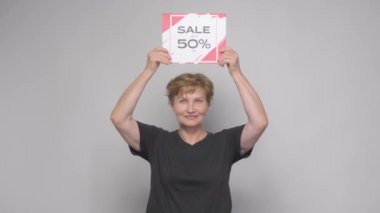 Yaşlı bir kadın% 50 indirim öneren bir satış afişi çeviriyor.
