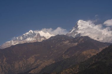 A breathtaking view of the snow-capped peaks of Annapurna I. and Annapurna South when the clouds softly hug the mountains in great Himalayas in Nepal.