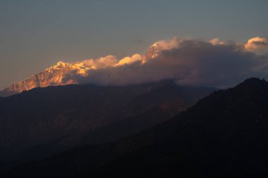 A breathtaking view of the snow-capped peaks of Annapurna I. and Annapurna South when the clouds softly hug the mountains in great Himalayas in Nepal.