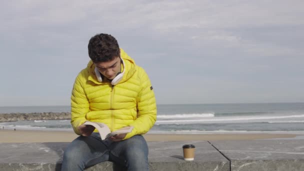 Ισπανόφωνος Νεαρός Διαβάζει Ένα Βιβλίο Στην Παραλία — Αρχείο Βίντεο