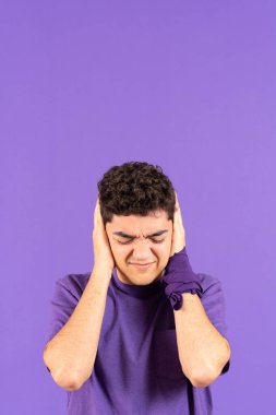 Hispanic boy with stress covering ears isolated on purple background with copy space. Feminism concept