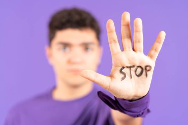 Stop message on hand of hispanic young man isolated on purple background