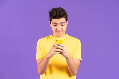 Front view of hispanic teenager boy using phone isolated on purple background