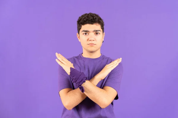 Hispanic teenager boy saying no with hands isolated on purple background. Feminism and gender violence concept