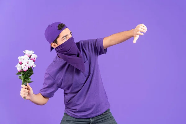 Young male unrecognizable protestor throwing flowers to enemy isolated on purple background. Feminism and equality concept. Man fighting for woman rights