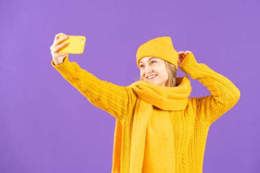 Winter clothing woman taking selfie on phone isolated on purple background