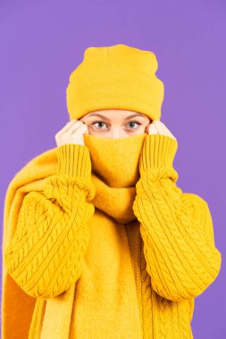 Winter clothing unrecognizable woman covering face with scarf while looking at camera isolated on purple background