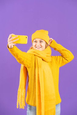 Winter clothing woman posing and taking selfie isolated on purple background.