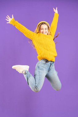 Full length studio shot of happy pretty young woman jumping on air isolated on purple background