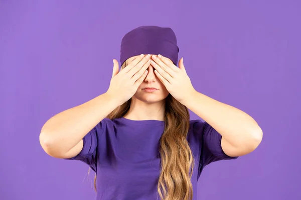 Young feminist woman covering eyes isolated on purple background. Gender violence concept