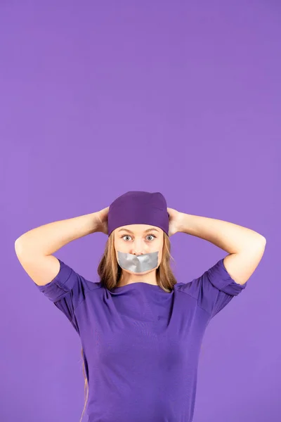 Worried young woman hands on head with adhesive tape on mouth isolated on purple background. Feminism concept